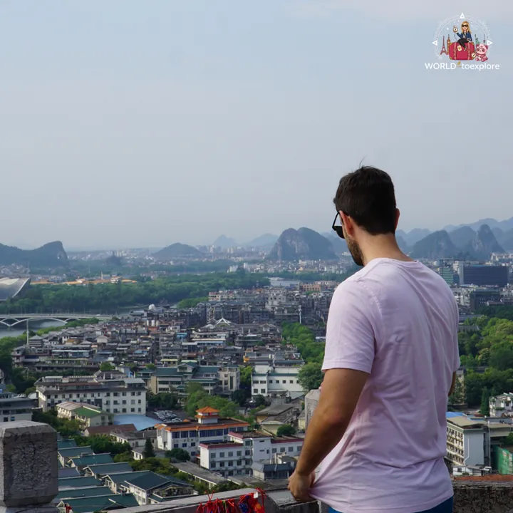 Man looking out over Guilin from the top of the hill, with the river and karst mountains in the background