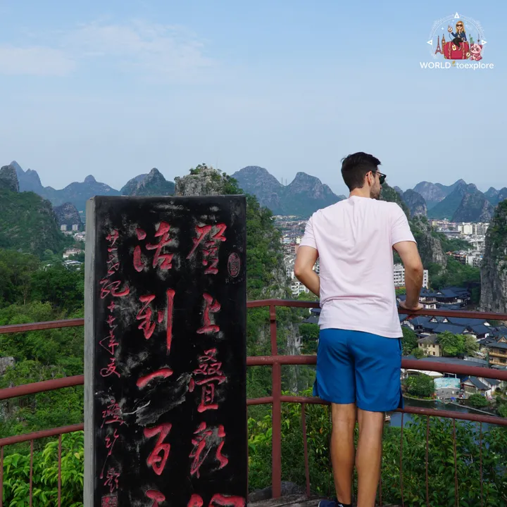 Man looking at a rock with an old inscription carved into it, with Guilin's karst mountains in the background