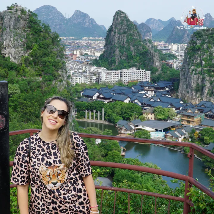 Cristina smiling by the viewpoint railing, with karst mountains and a traditional Chinese village in the background