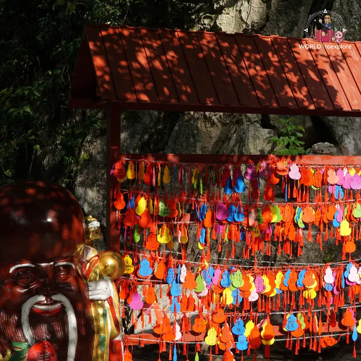 Colourful gourd charms hanging near a cave, with a golden statue in the foreground
