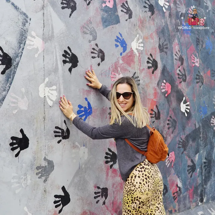 Hands resting on a stretch of the wall covered with dozens of painted handprints in black, white, blue and pink
