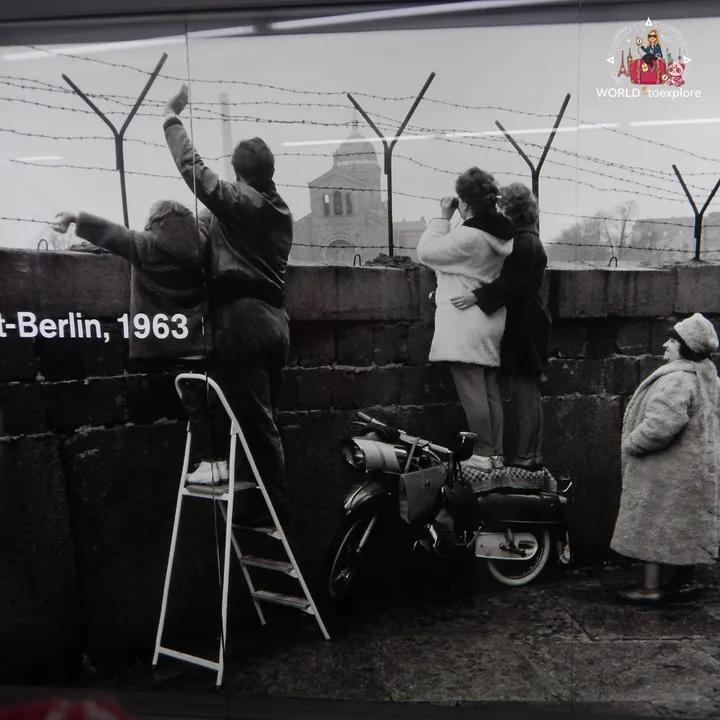 A large 1963 photograph in the exhibition, showing people standing on ladders and on a motorbike to look over the wall