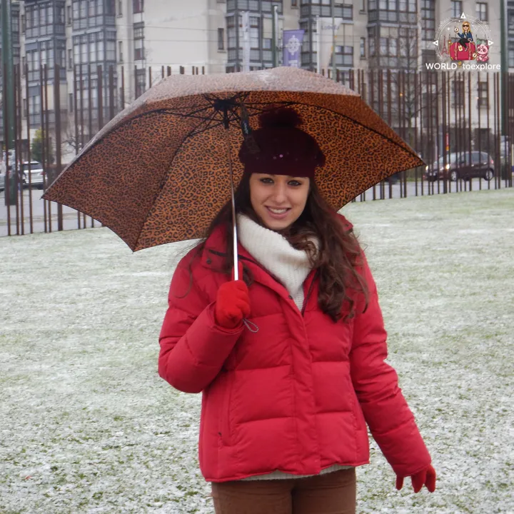 Holding an umbrella on the memorial's snow-covered grass, with the iron posts of the wall's old course behind