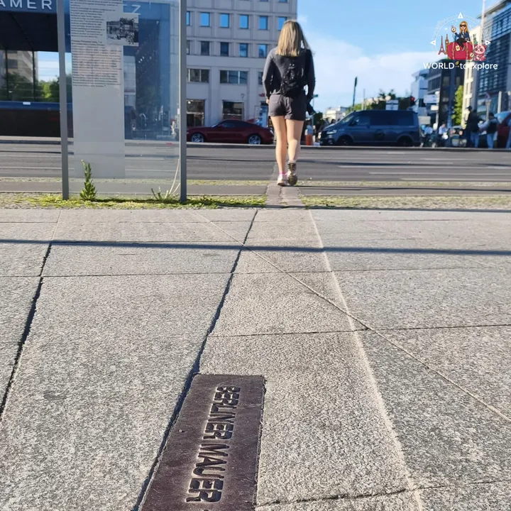 The metal plaque reading Berliner Mauer set into the pavement, with the information panel and the avenue behind