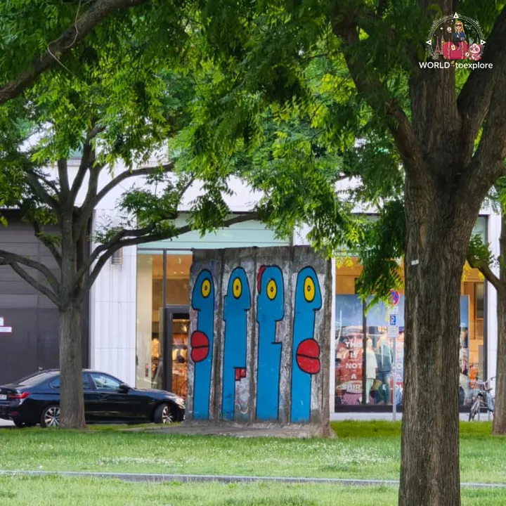 Stretches of the wall painted with four blue heads, standing on a lawn beside a street with shops