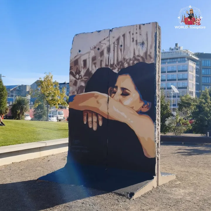 A stretch of the wall painted with two people embracing, standing outdoors in a garden with modern buildings behind