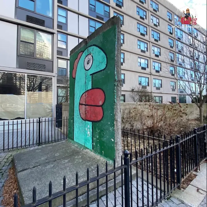 A stretch of the wall painted with a green head, protected by railings, in front of a tall building with square windows