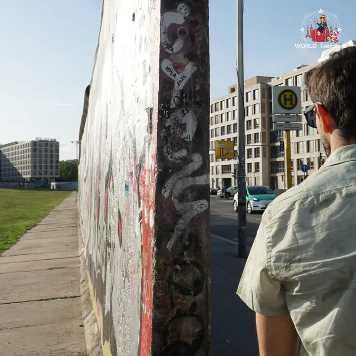 Looking at the side of a stretch of the wall at the East Side Gallery, with the city's modern buildings across the road