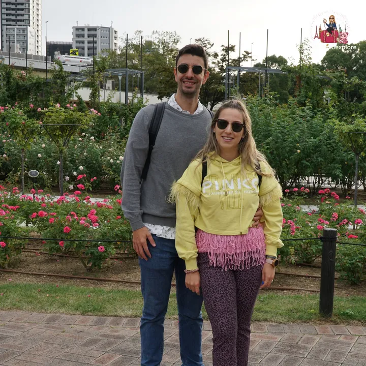 Smiling couple at the Nakanoshima Rose Garden in a closer shot, with roses and buildings in the background