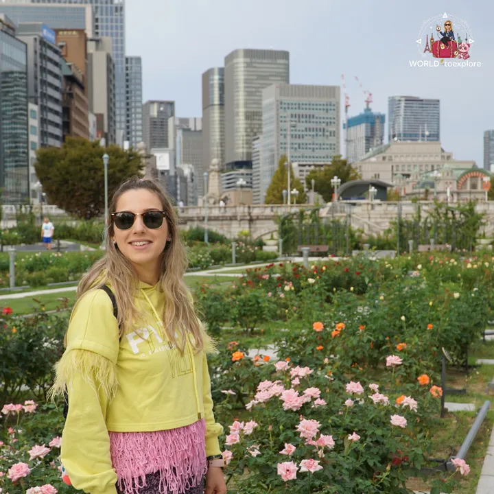 Smiling woman at the Nakanoshima Rose Garden, with colourful roses and the Osaka skyline behind