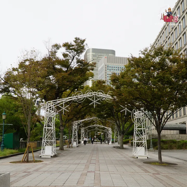 Tree-lined path in Nakanoshima with white decorative arches, next to modern Osaka buildings