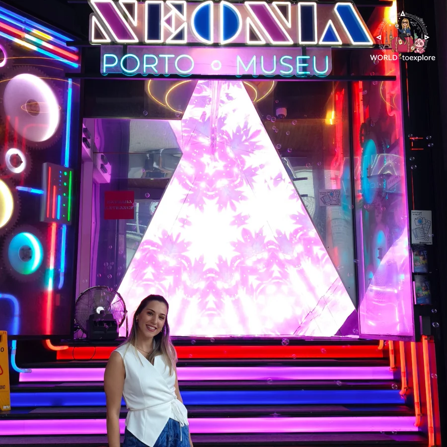 Cristina in a white top in front of the entrance to Neonia, in Porto, with the 'Neonia Porto Museu' sign and pink and blue neon lights