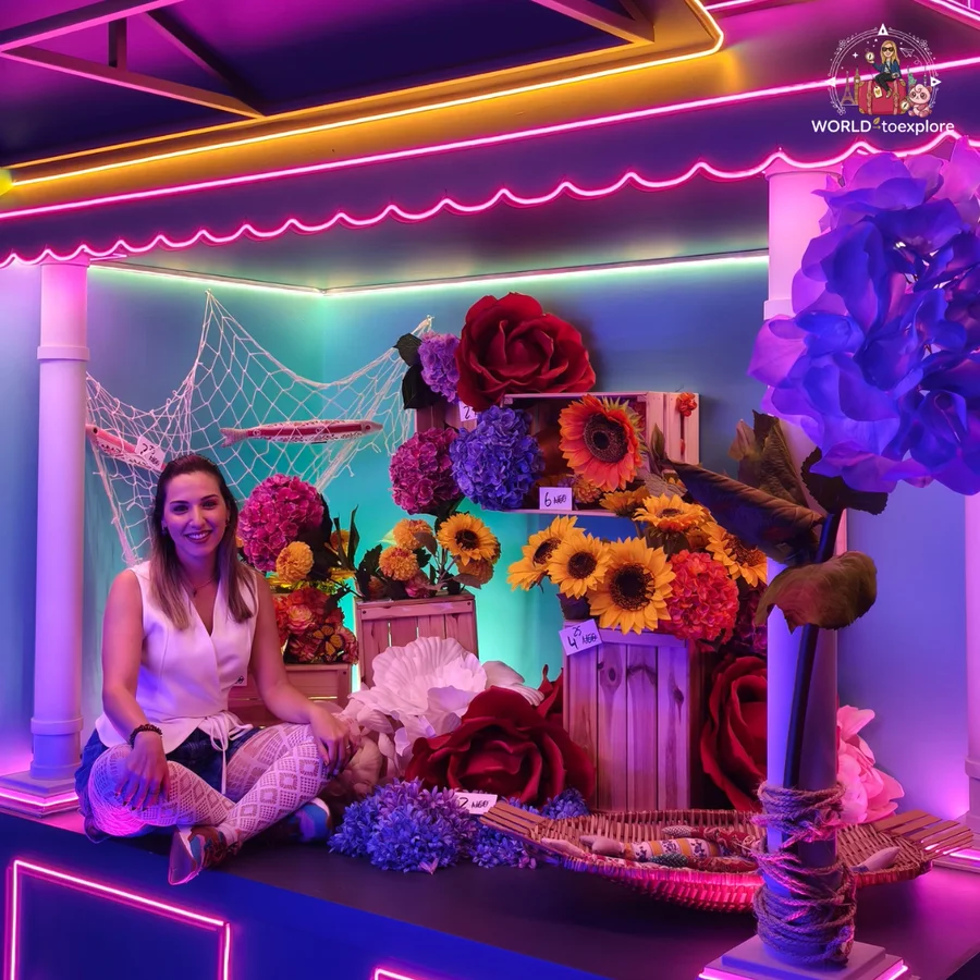 Cristina sitting on the floor in a set with flowers, sunflowers and fishing nets, in a room at Neonia inspired by a flower market