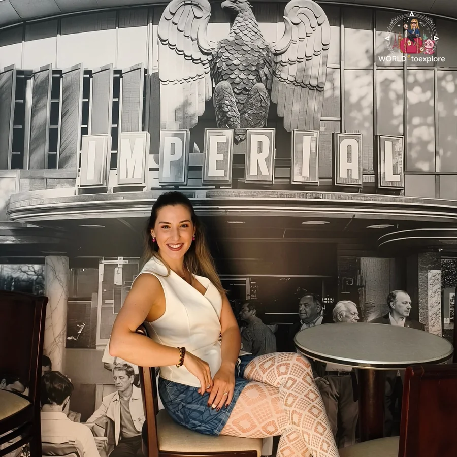 Cristina sitting at a café table in front of an old black-and-white façade with the word 'Imperial' and an eagle, at Neonia