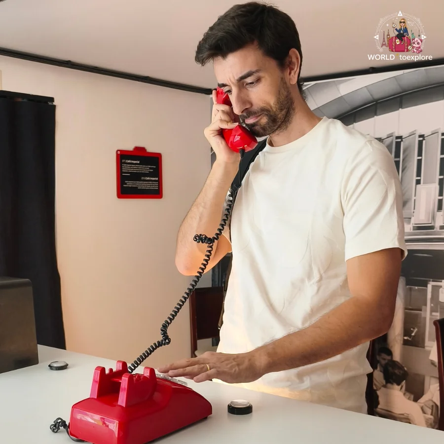 Her husband answering a red rotary telephone, in a room at Neonia with old black-and-white photographs