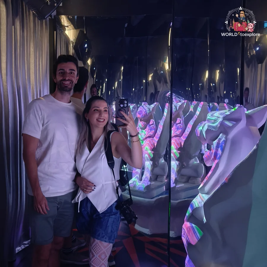Cristina and her husband taking a selfie in a mirrored corridor with reflected sculptures, at Neonia