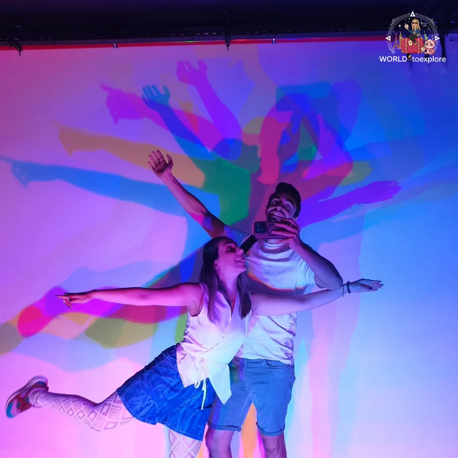 Cristina and her husband striking funny poses, with coloured shadows projected on the wall, in a room at Neonia