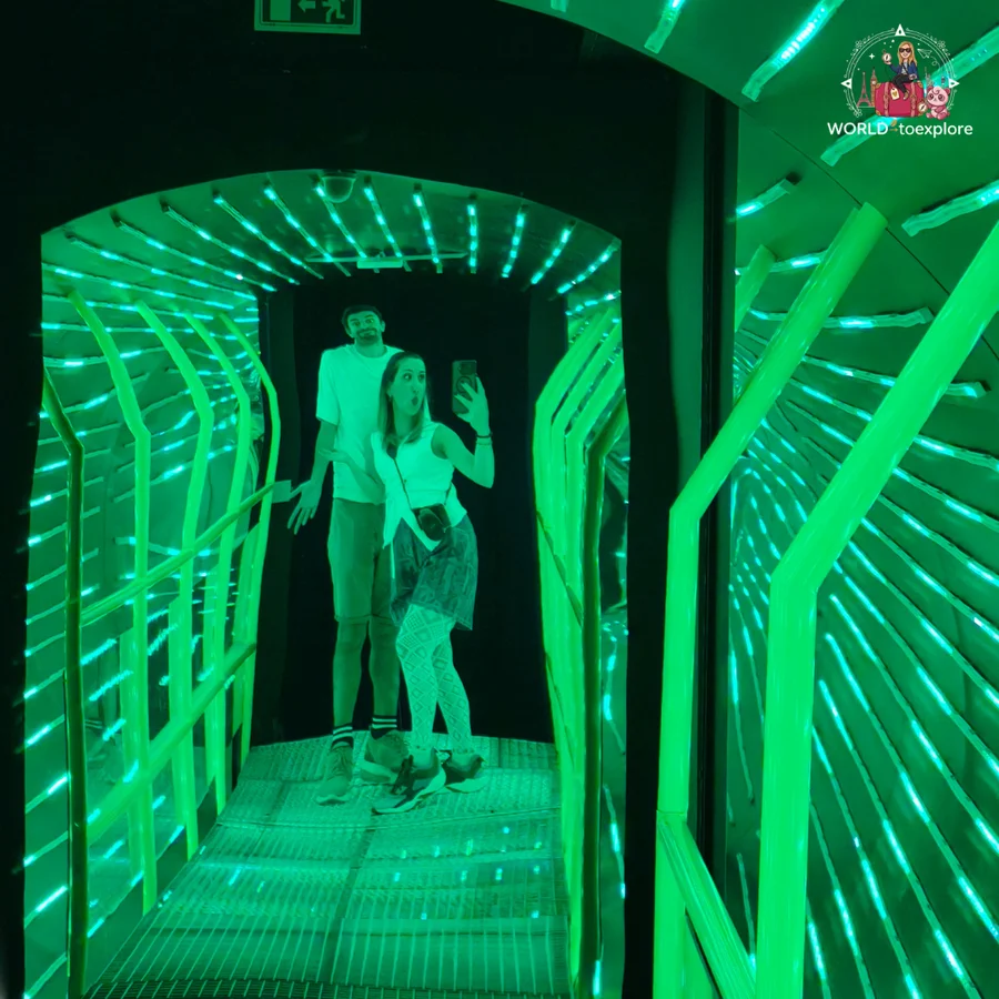 Cristina and her husband in a corridor lit with green neon lights at Neonia, while she takes a photo in the mirror