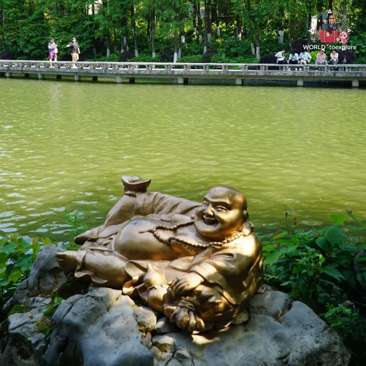 Golden statue of a smiling Buddha by a lake, surrounded by greenery