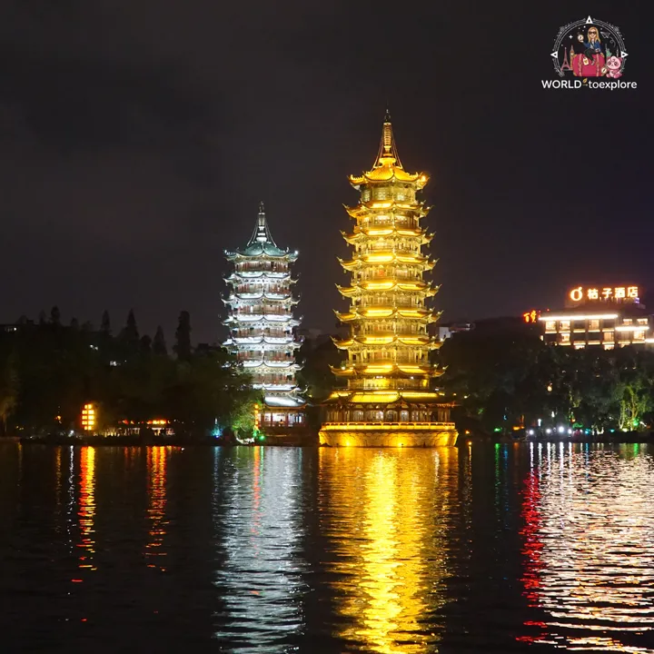 The Sun and Moon Pagodas lit up at dusk, one in white and the other in gold, reflected in the lake