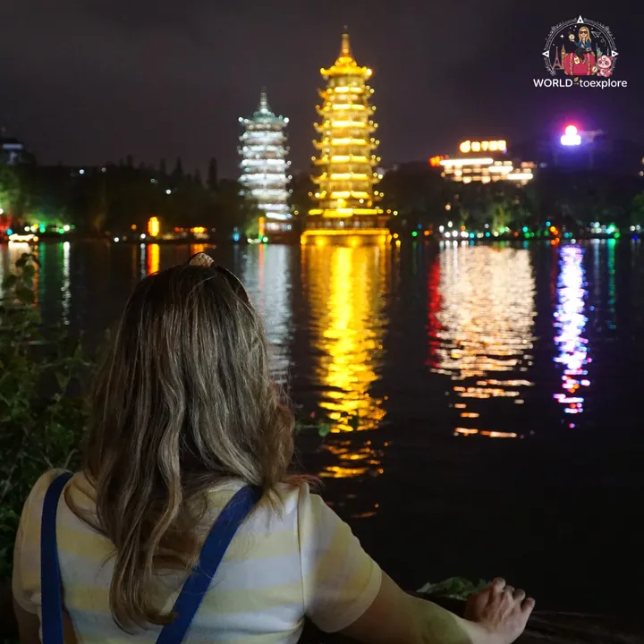 Cristina from behind, looking at the two pagodas lit up at night, reflected in the lake