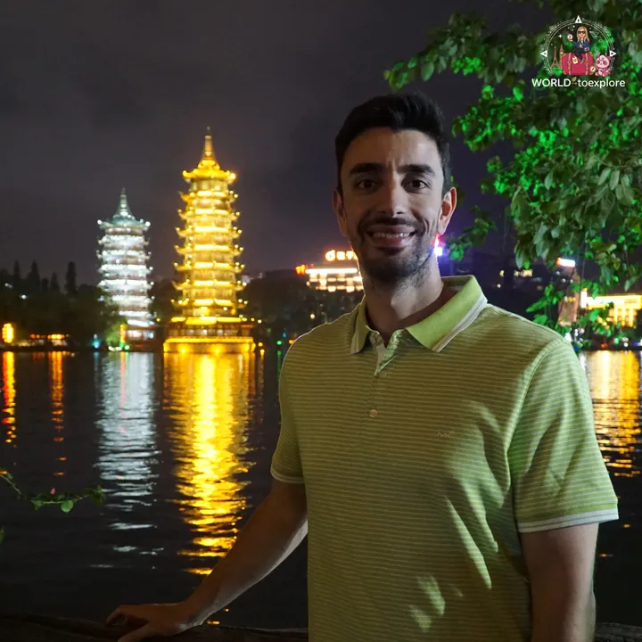 Man smiling with the two lit-up pagodas in the background, at night