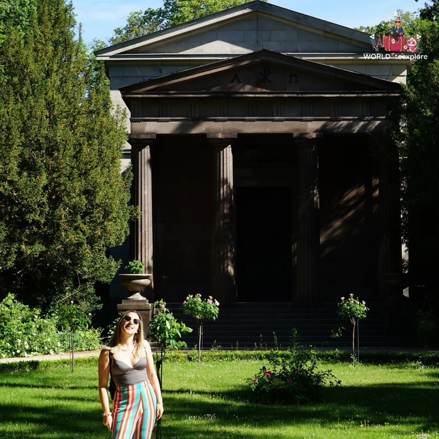 Woman next to the Mausoleum, a classical building with columns and a pediment, surrounded by garden