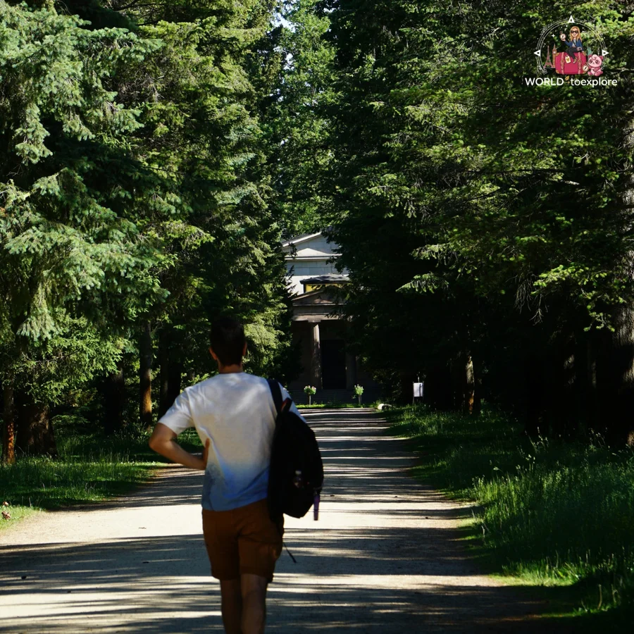 Man seen from behind walking along a dirt path between trees towards the Mausoleum