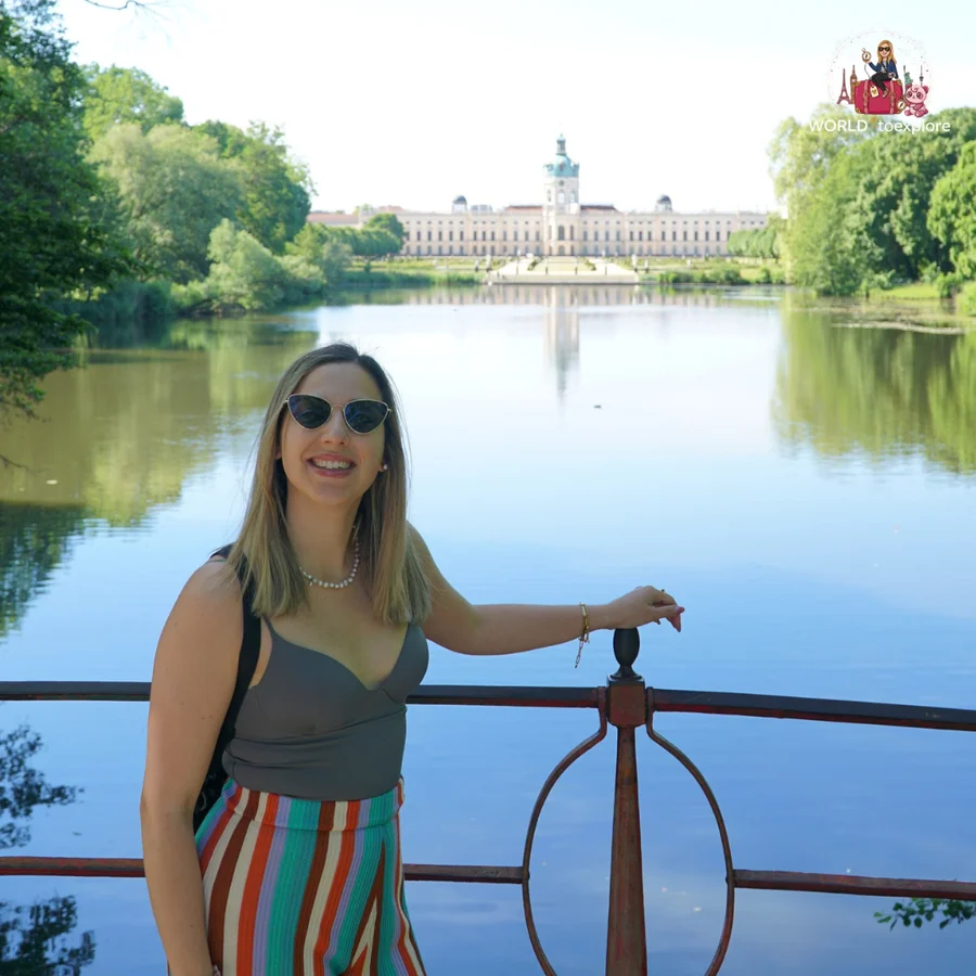 Smiling woman leaning on a railing by the lake, with the palace in the distance