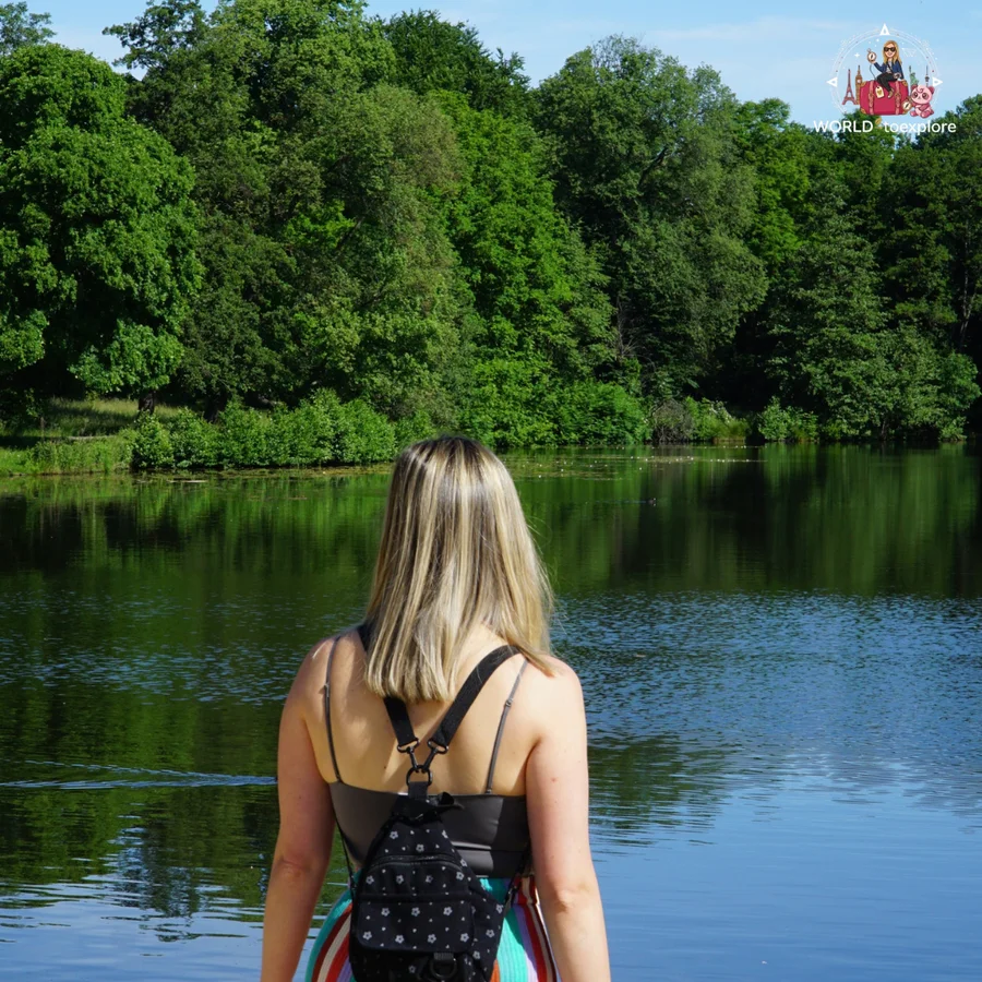 Woman seen from behind, with a backpack, looking at the lake surrounded by trees