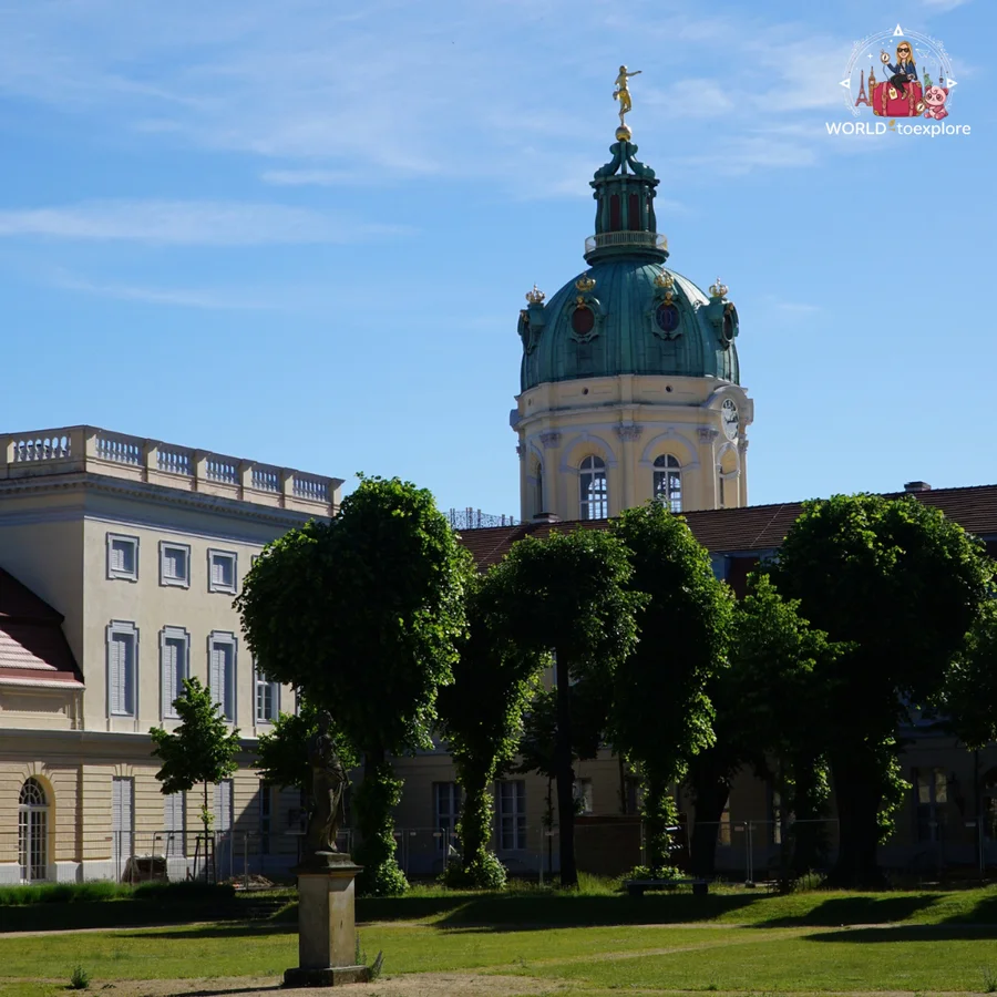 Green dome of Charlottenburg Palace rising above a row of trimmed trees, next to one of the yellow wings