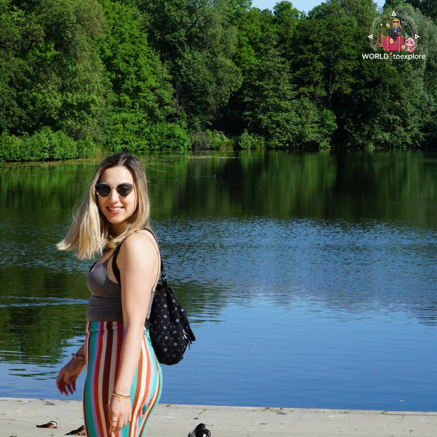 Smiling woman by the lake, her hair blowing in the wind, with green woodland behind her