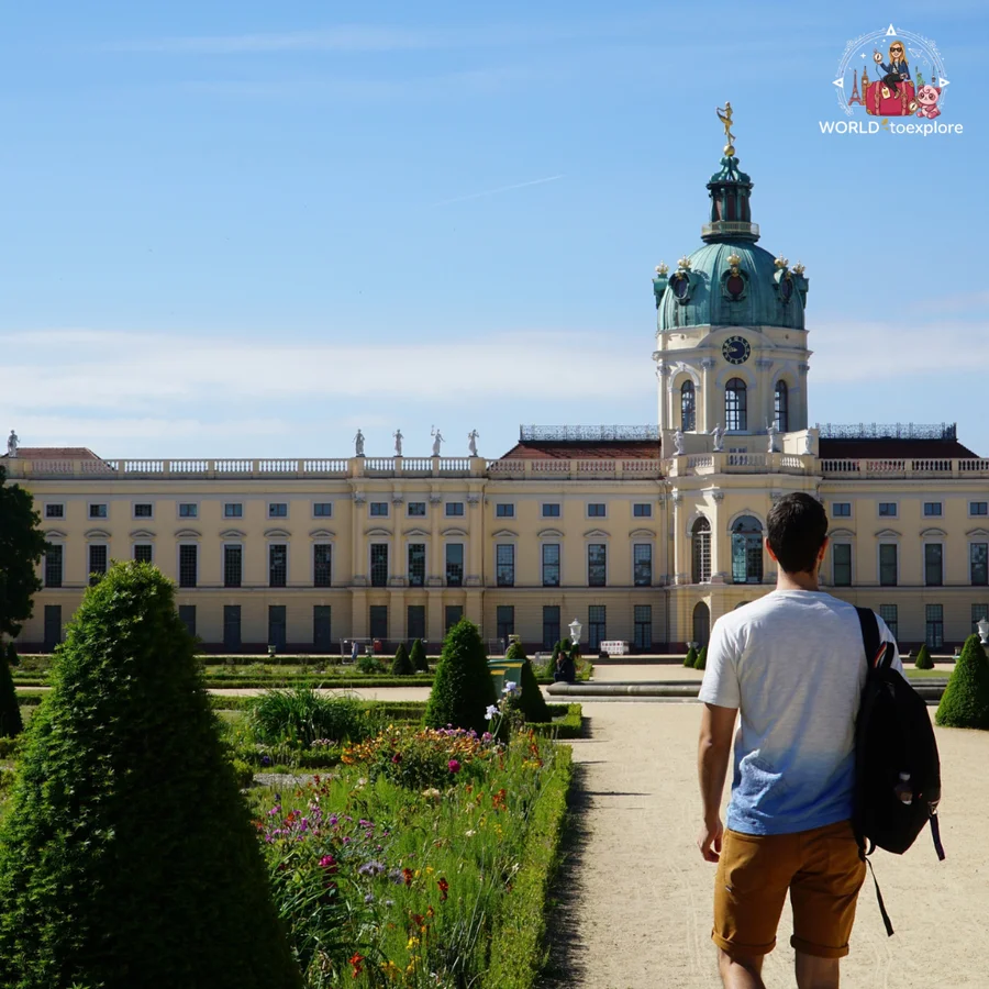 Man seen from behind in the formal gardens, between flower beds and trimmed shrubs, with the palace dome in the background