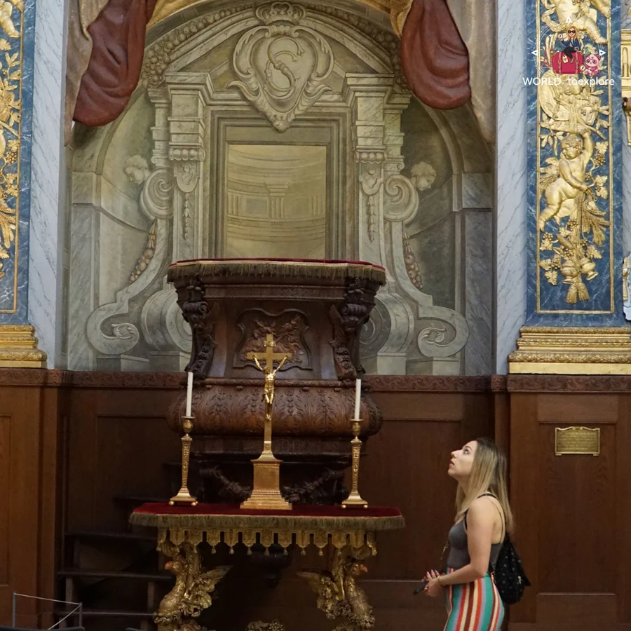 Woman looking at an ornate wooden altar with golden details and a crucifix, in a room of the palace