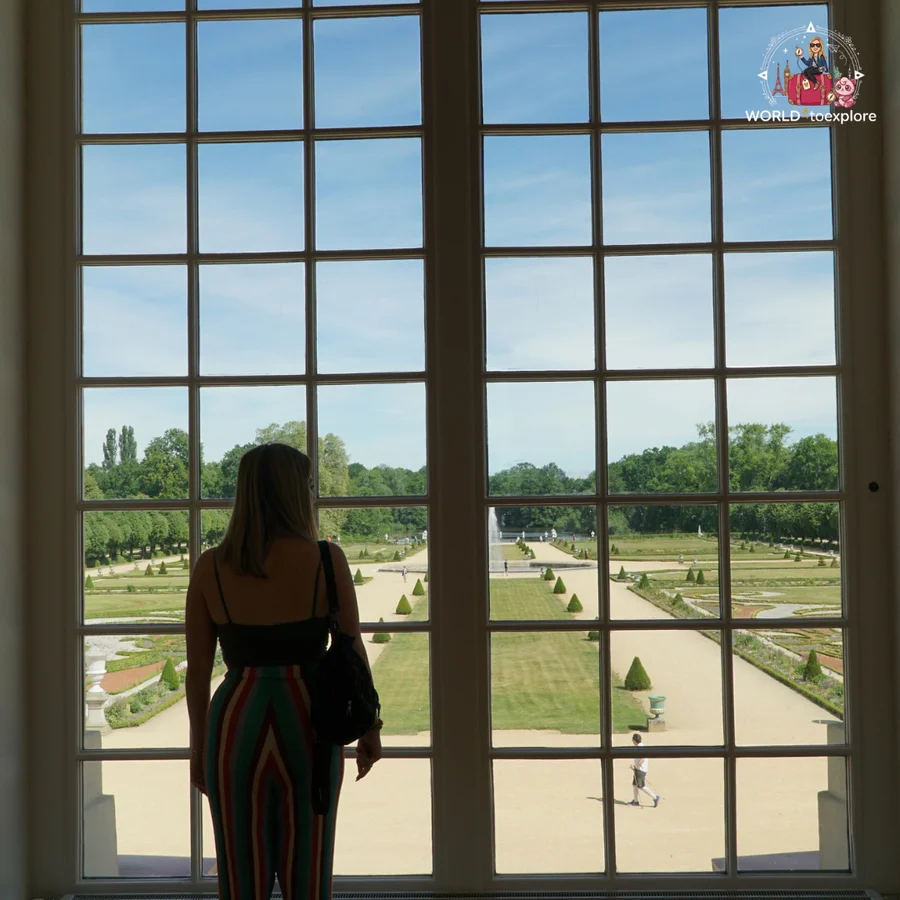 Woman seen from behind in front of a large window, with a view over the palace gardens