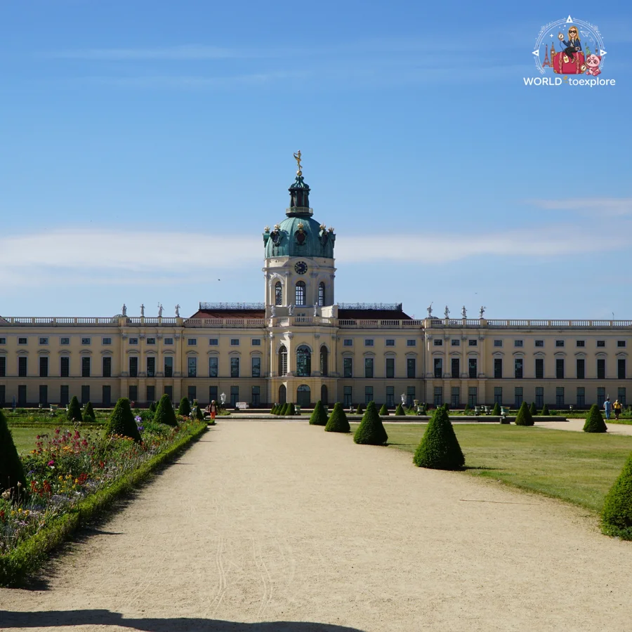 Formal garden at Charlottenburg with flower beds and trimmed shrubs, and the palace with its green dome in the background