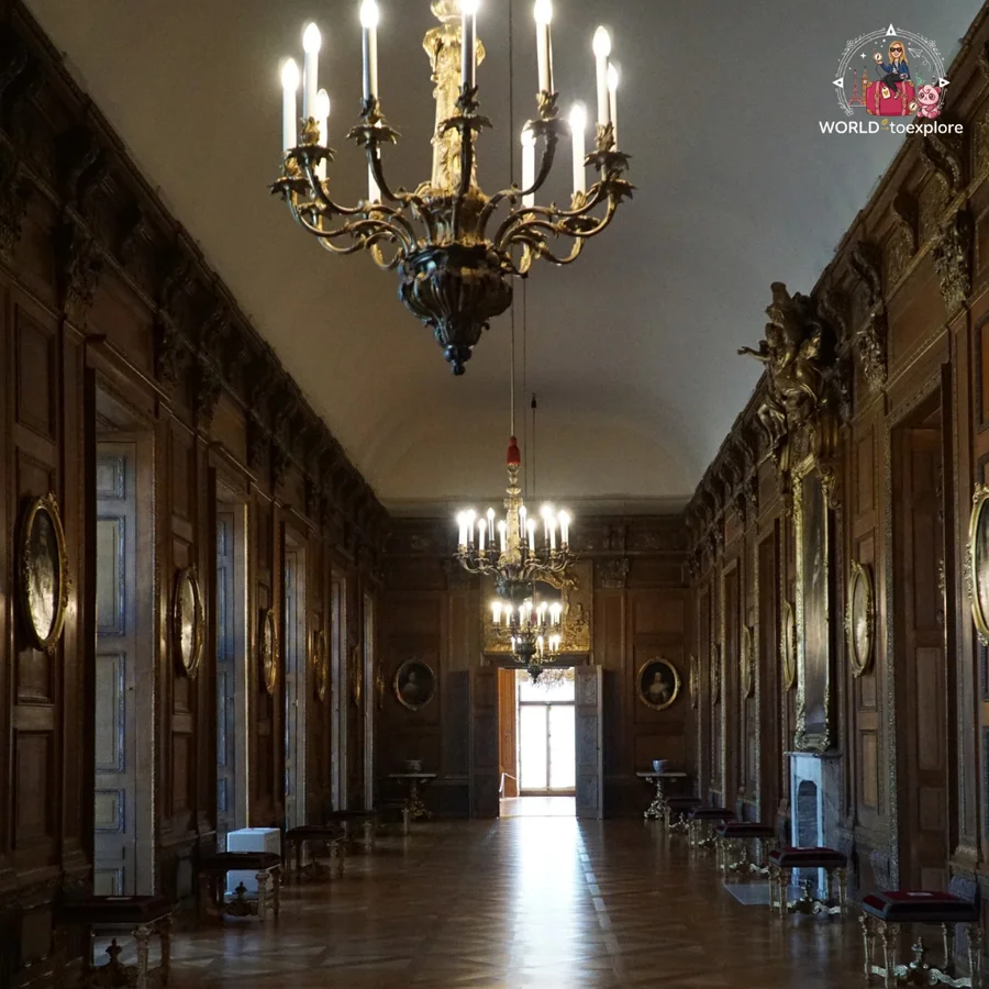 Long gallery with dark wood panelling, candle chandeliers and a bright doorway at the end