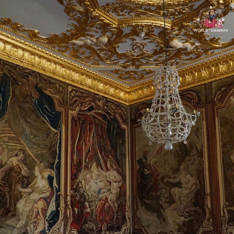 Corner of a room with an intricate golden ceiling, a crystal chandelier and tapestries on the walls