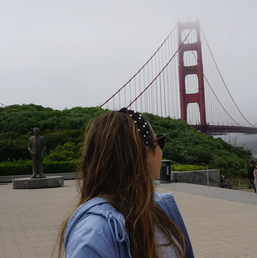 The author looking towards the Golden Gate Bridge next to the Joseph Strauss statue, with the bridge tower peeking through the fog
