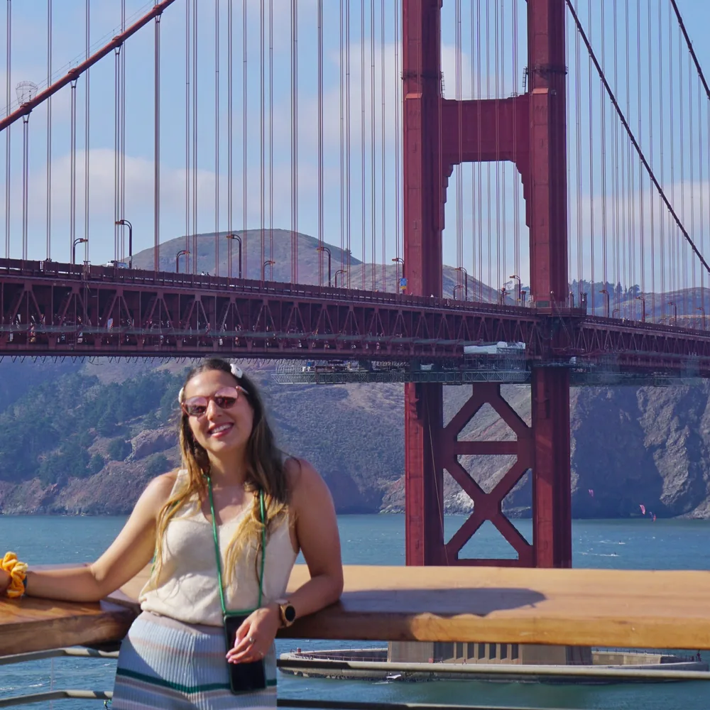 The author leaning on a wooden railing at the Golden Gate Postcard Viewpoint on a clear day, with the bridge tower behind her