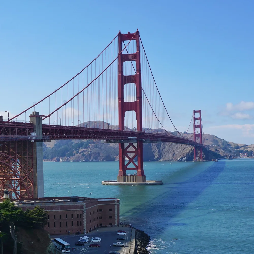 A panoramic view of the Golden Gate Bridge from above, with Fort Point and the car park next to the water