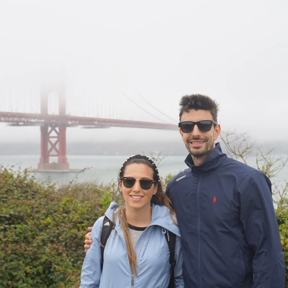 A couple posing at the Golden Gate Viewpoint, with one of the bridge's towers wrapped in fog behind them