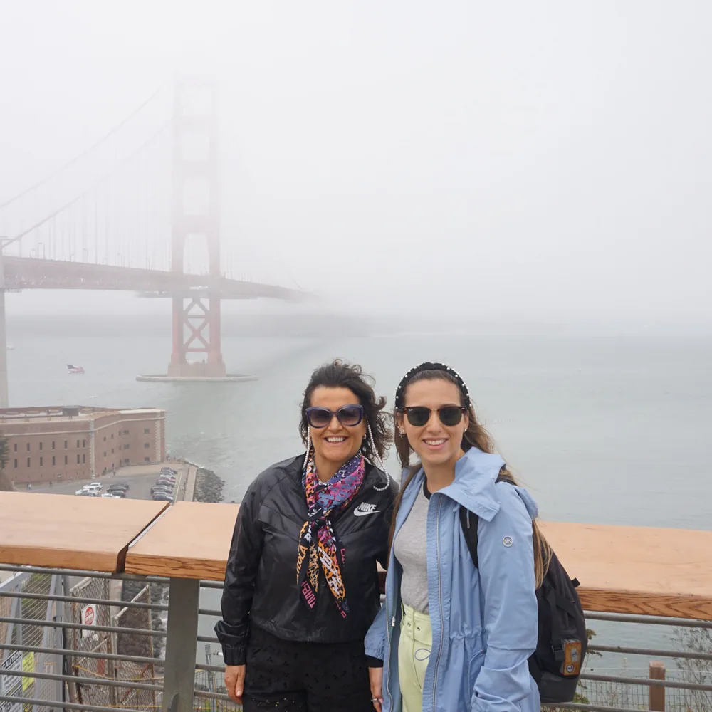 The author and her mother posing at a lookout over the bay, with the fog-covered Golden Gate Bridge and the Fort Point Building below