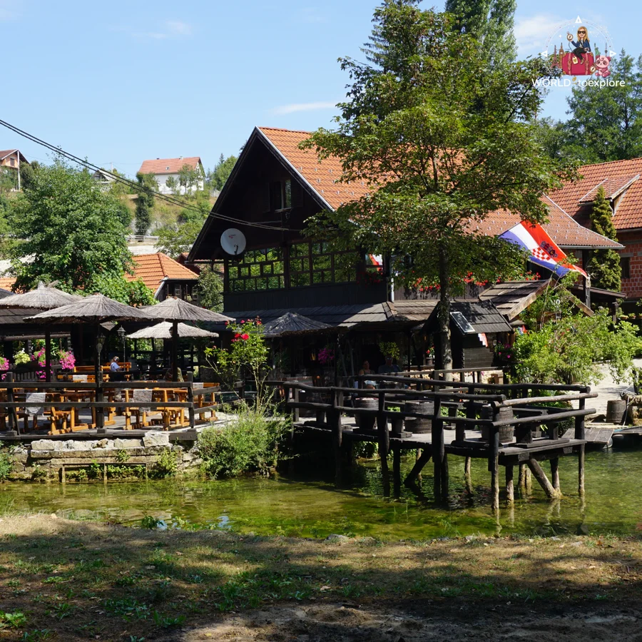 Wooden terraces over the water in Rastoke, with thatched umbrellas, the Croatian flag and red-roofed houses