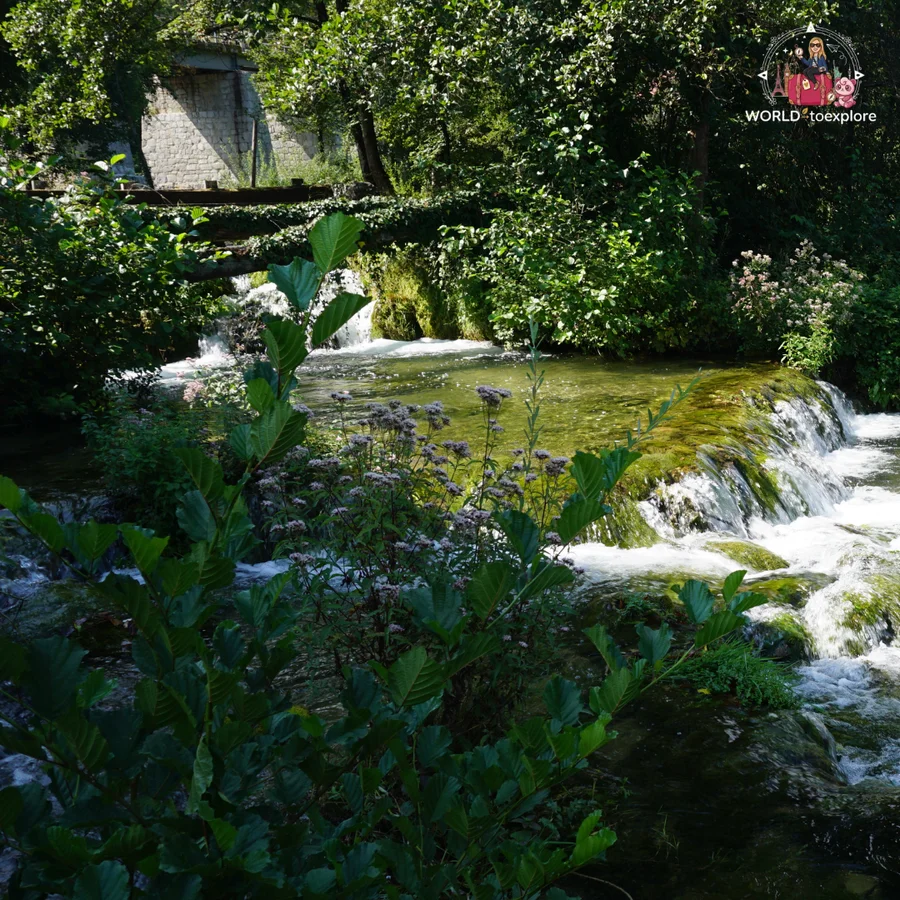 Cascades of the Slunjčica among dense greenery in Rastoke, with a wooden bridge behind
