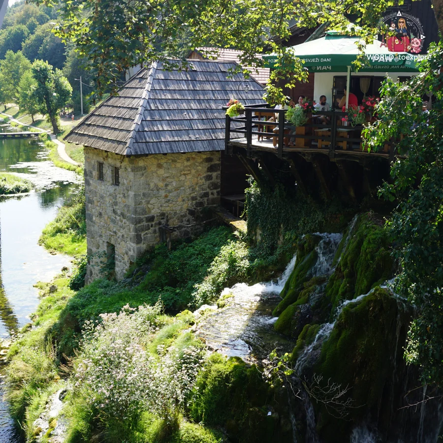 Stone mill with a wooden shingle roof in Rastoke, with waterfalls tumbling down the moss-covered rock and a terrace alongside