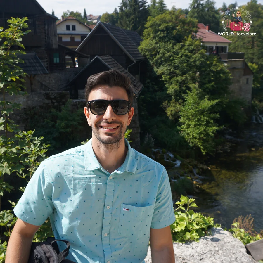 Cristina's partner smiling, with the wooden mills and the waterfalls of Rastoke behind