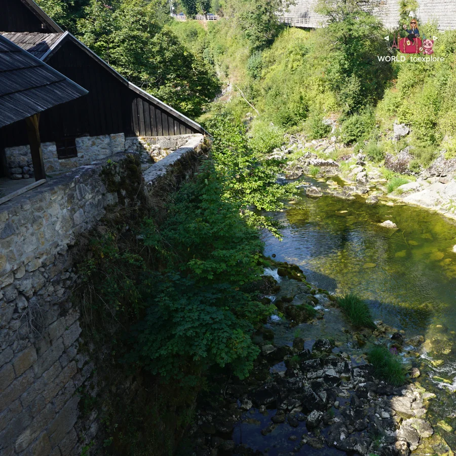 Wooden house on a stone wall in Rastoke, with the clear river and its rocky bed below