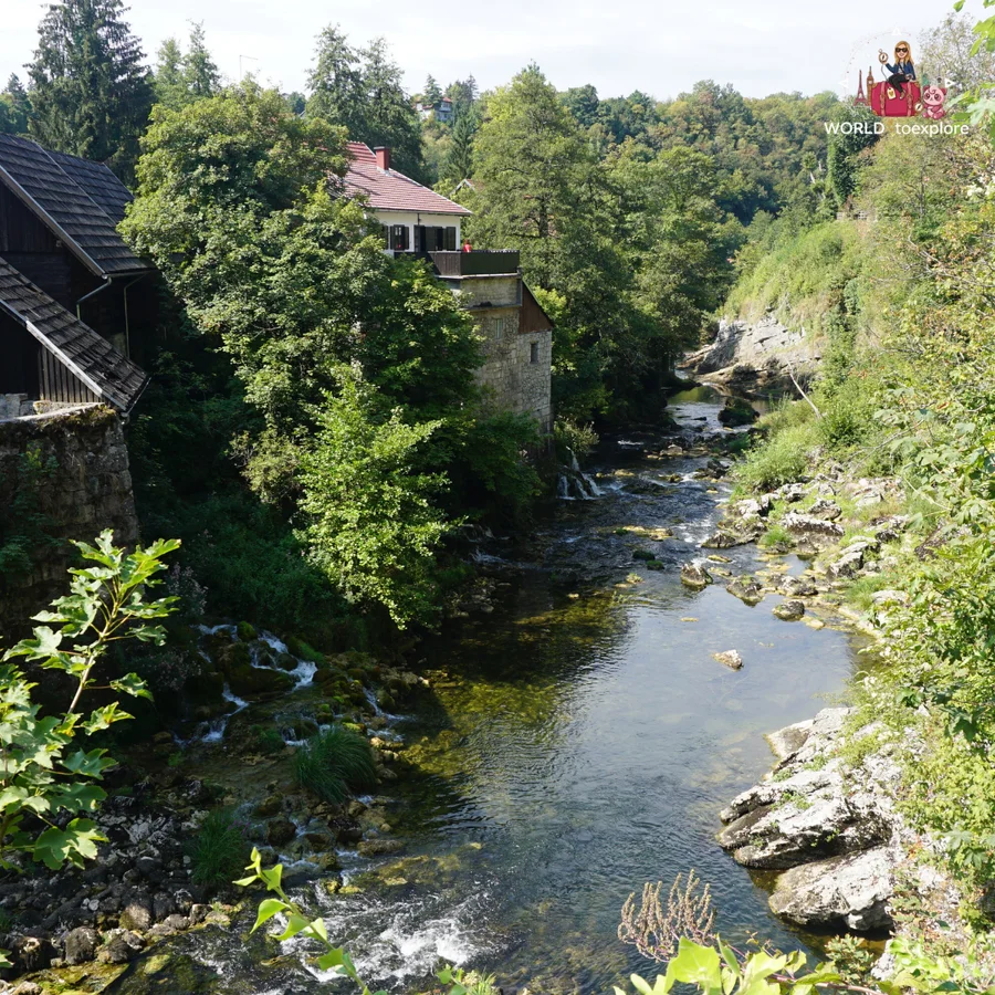 River valley seen from above in Rastoke, with stone and wooden houses among the greenery and small falls along the banks