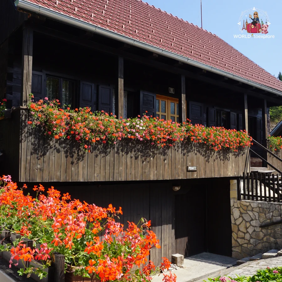 Traditional Rastoke house in dark wood, with a red tiled roof and a balcony full of red geraniums